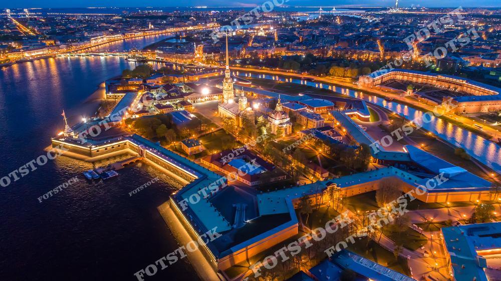 На фотографии изображена Петропавловская крепость — одно из древнейших сооружений Санкт-Петербурга, расположенное на Заячьем острове. Ночная подсветка подчеркивает стены, башни и знаменитый золотой шпиль собора святых Петра и Павла, возвышающийся над крепостью. Вдалеке видны огни набережной и мостов, создающие атмосферу спокойного ночного Петербурга. Эта панорама символизирует историческое сердце города, объединяя архитектурную красоту и значимость крепости.